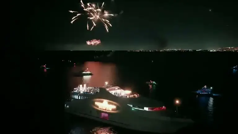 Fireworks over a lit yacht on dark water.