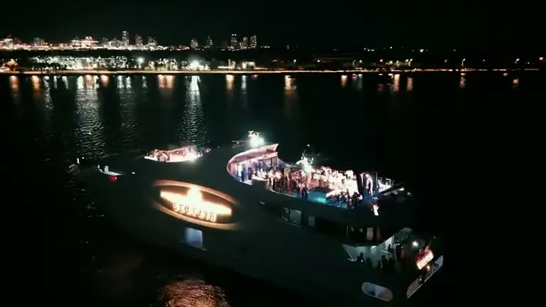 A yacht lit up on the bay, the skyline behind it.